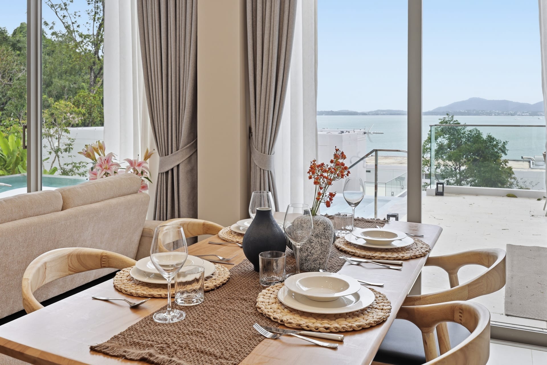 The dining table set for four against floor-to-ceiling glass, the Andaman Sea filling the view behind