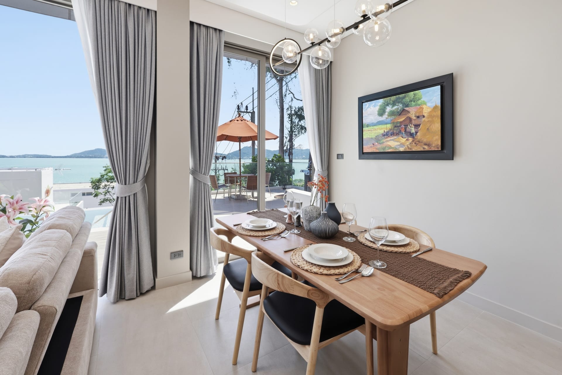 The dining table set for a meal, sheer curtains framing the sliding glass and the bay