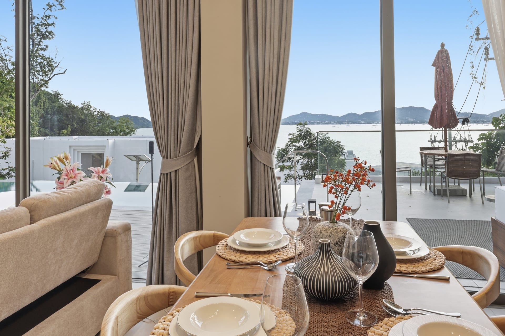 The dining table and great-room sofa with an orange parasol on the terrace and the bay beyond the glass