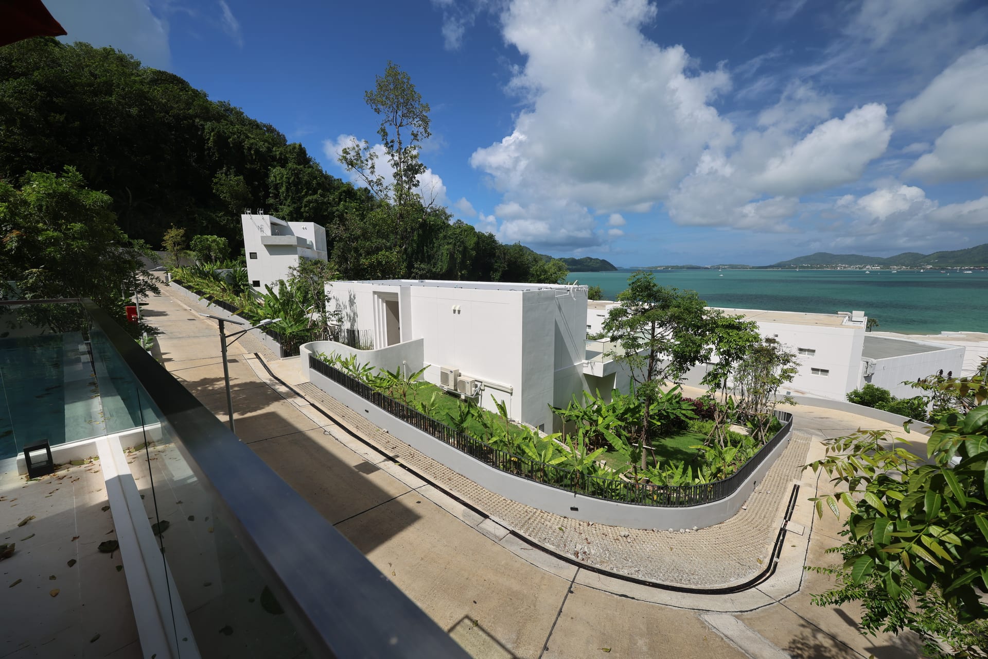 Wide daytime view down the access road of the villa row at Veranda Sea View Suite, with the infinity pool on the left and the bay opening to the horizon on the right