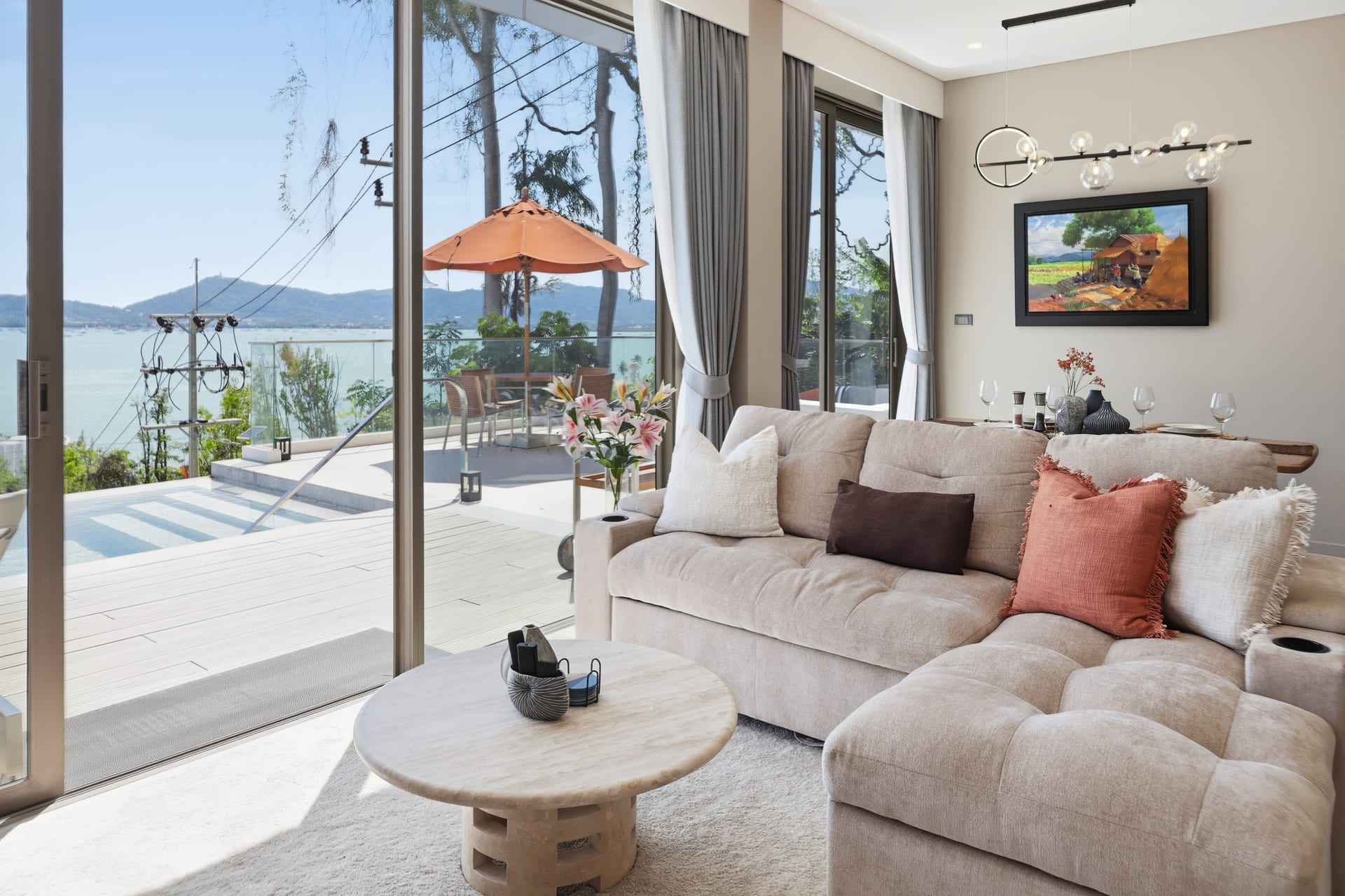 The great room's corner seating with round tables and framed art, sliding doors to the terrace, pool and bay
