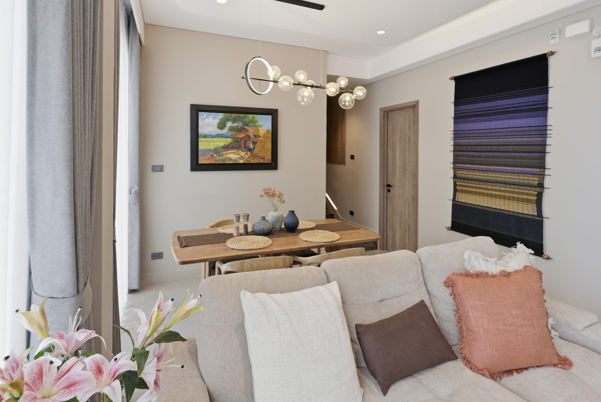 Open-plan great room and dining area — linen sofa, dining table and framed art under a sculptural pendant light