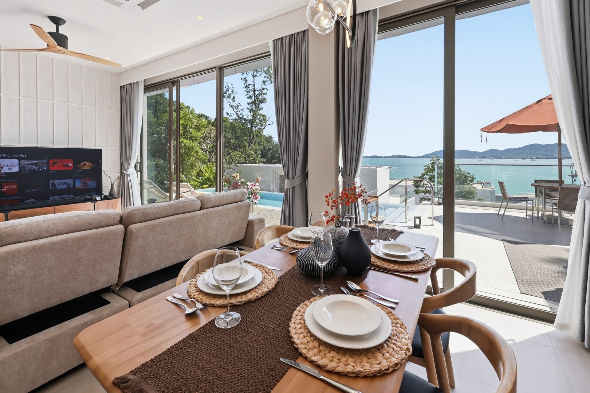 The open-plan great room with sofa, dining table and OLED TV, the sea view beyond the sliding glass