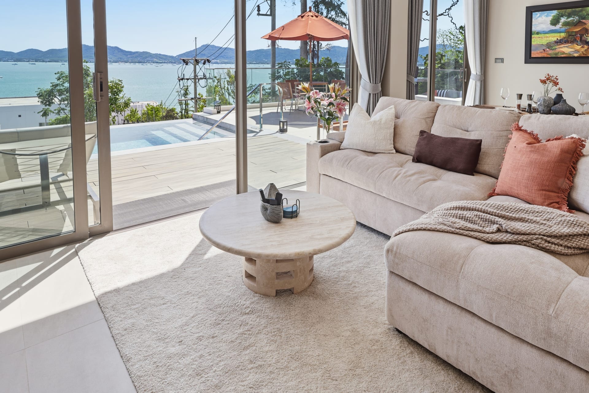 The great room with round teak tables and sliding doors to the pool terrace, an orange parasol and the bay beyond