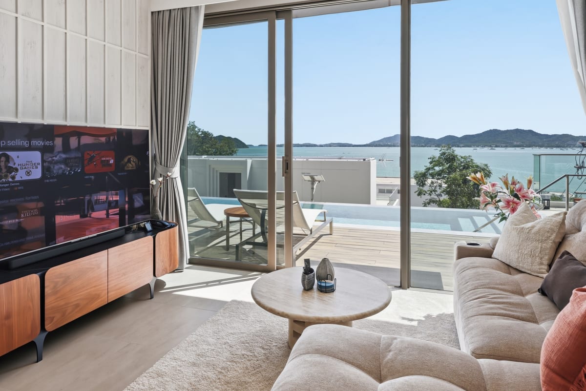 The great room with wall-mounted OLED TV, linen sofa and the bay view through the glass