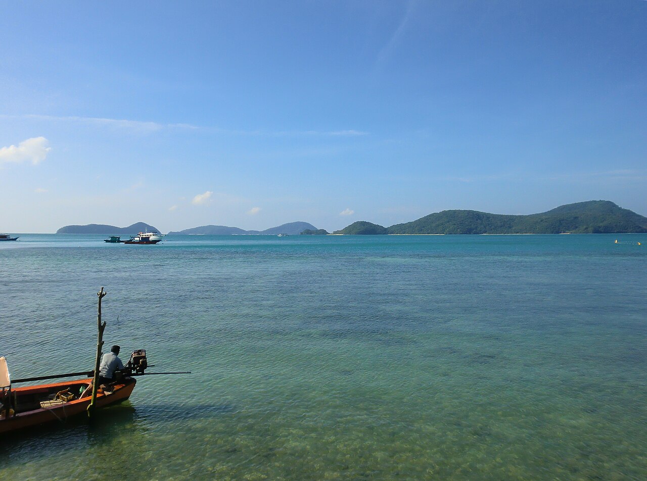 Calm Cape Panwa waters with a long-tail boat moored in the foreground and the green coastline curving out into the Andaman.