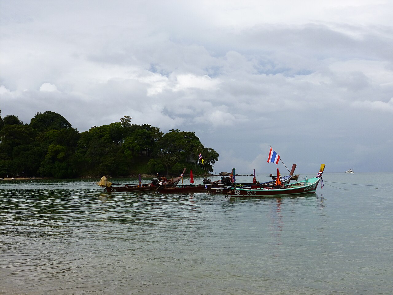 Long-tail boats moored along Patong Beach, looking south along the curved bay at dusk.