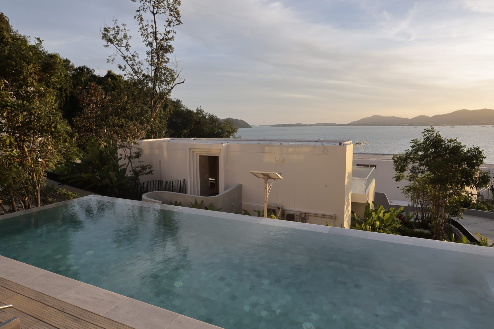 The infinity pool in soft golden-hour light, the white villa and Ao Yon Bay beyond the timber deck