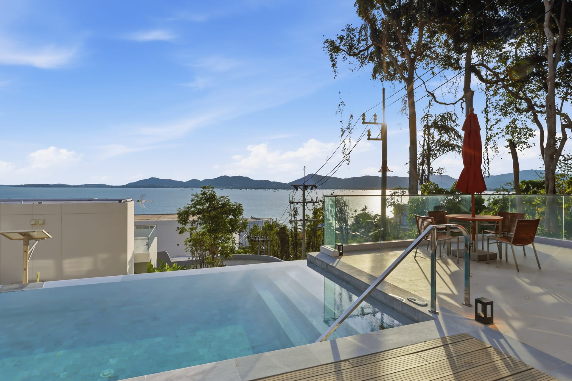 The pool deck with sun loungers and a dining set at the infinity edge, the bay beyond