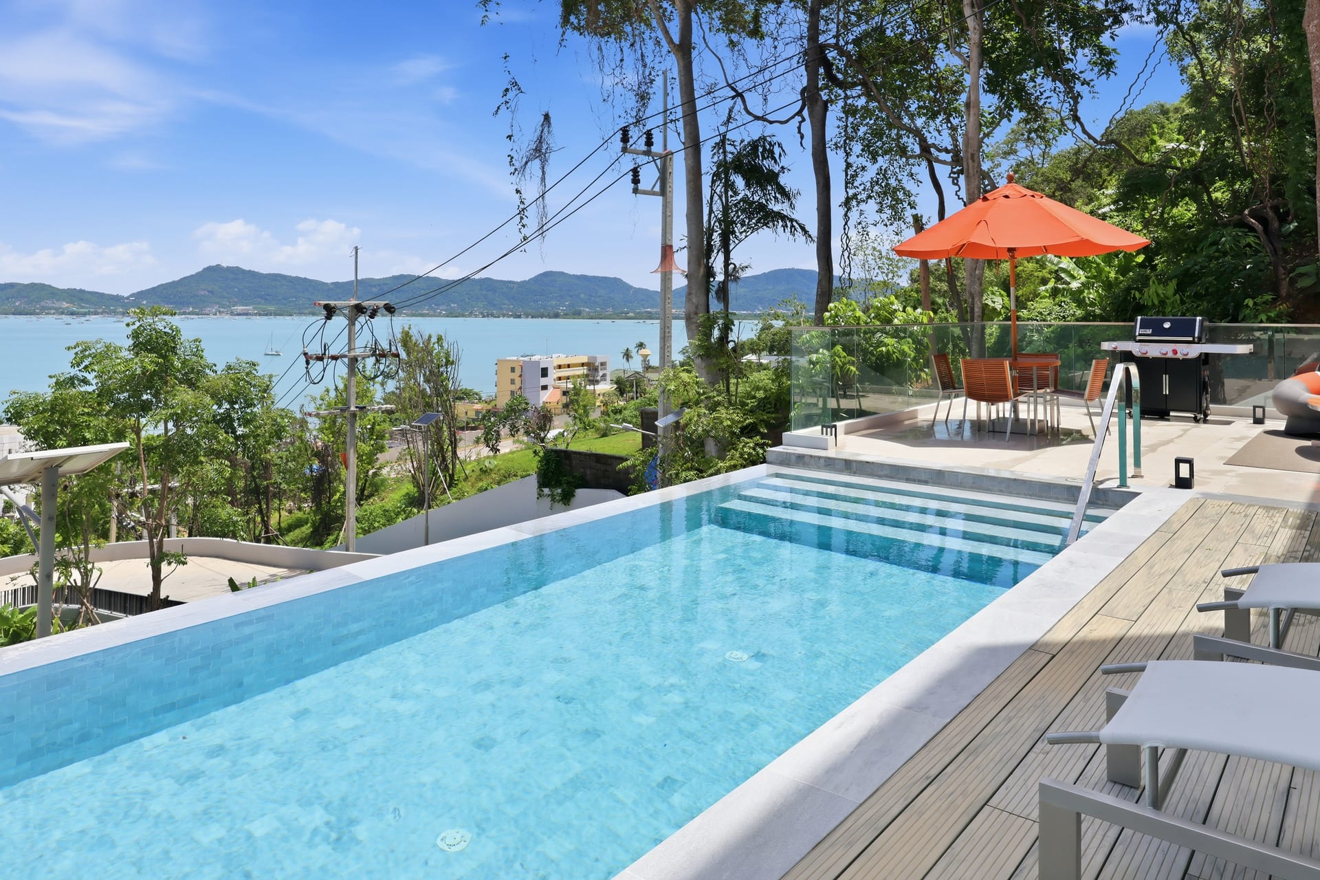 The infinity pool with an orange parasol and an al-fresco dining set on the deck, the bay opening to the horizon