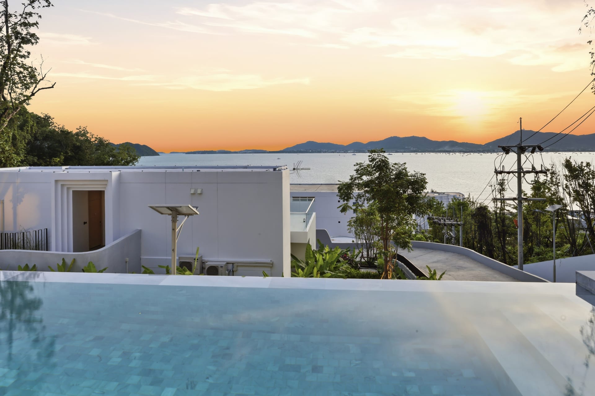 The infinity pool at sunset, golden light over the white villa and Ao Yon Bay, the Andaman beyond the deck