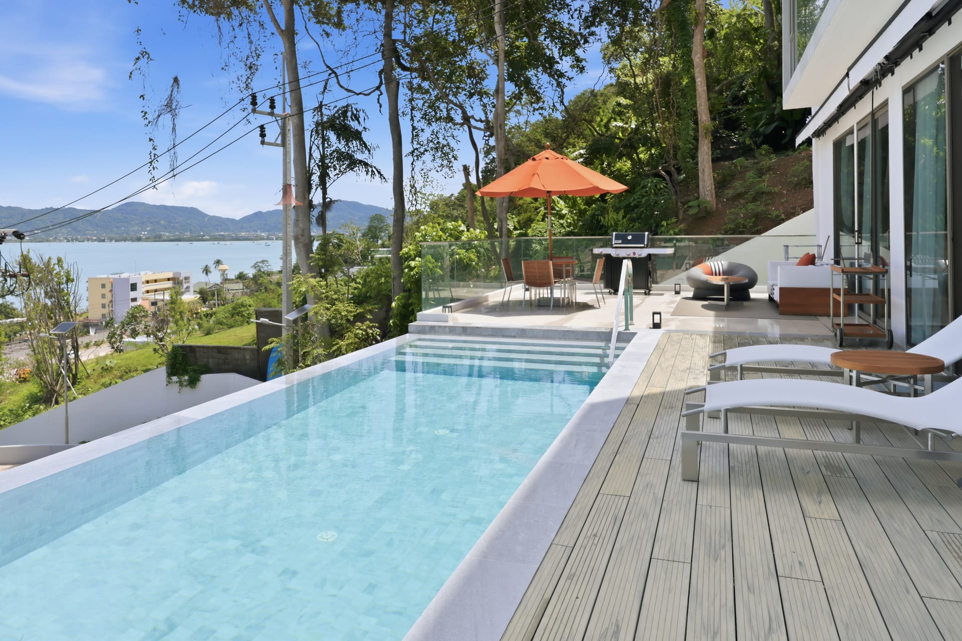 Teak sun loungers and an orange parasol beside the infinity pool, the Andaman and headlands in the background