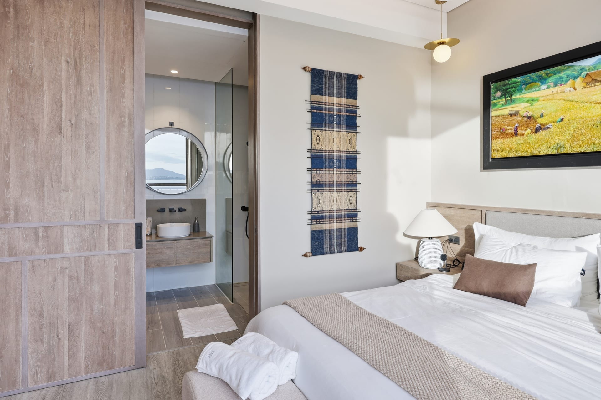The primary bedroom looking through to its ensuite bathroom with round mirror and vanity
