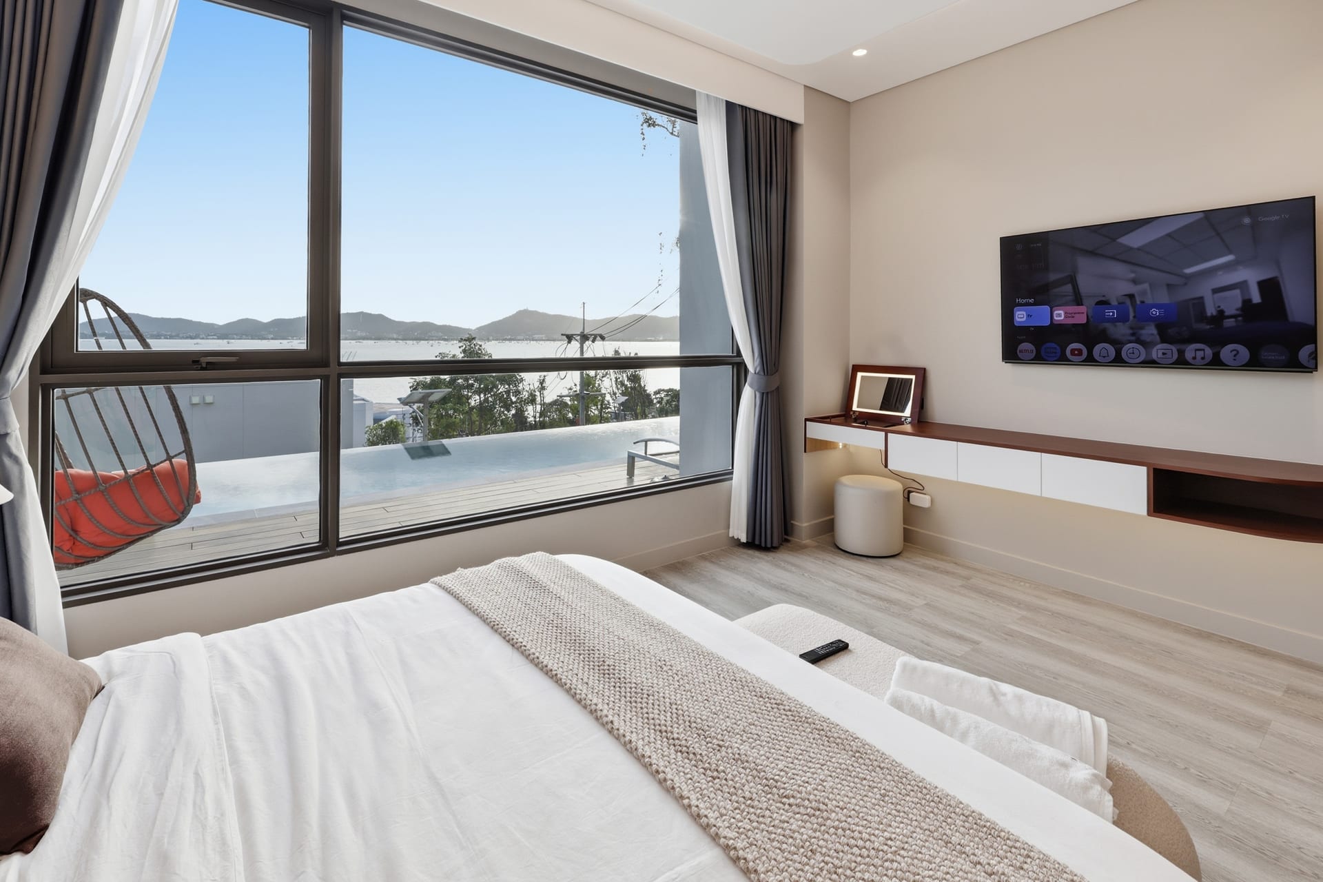 The primary bedroom's king bed and hanging chair with a wall-mounted TV and the bay view