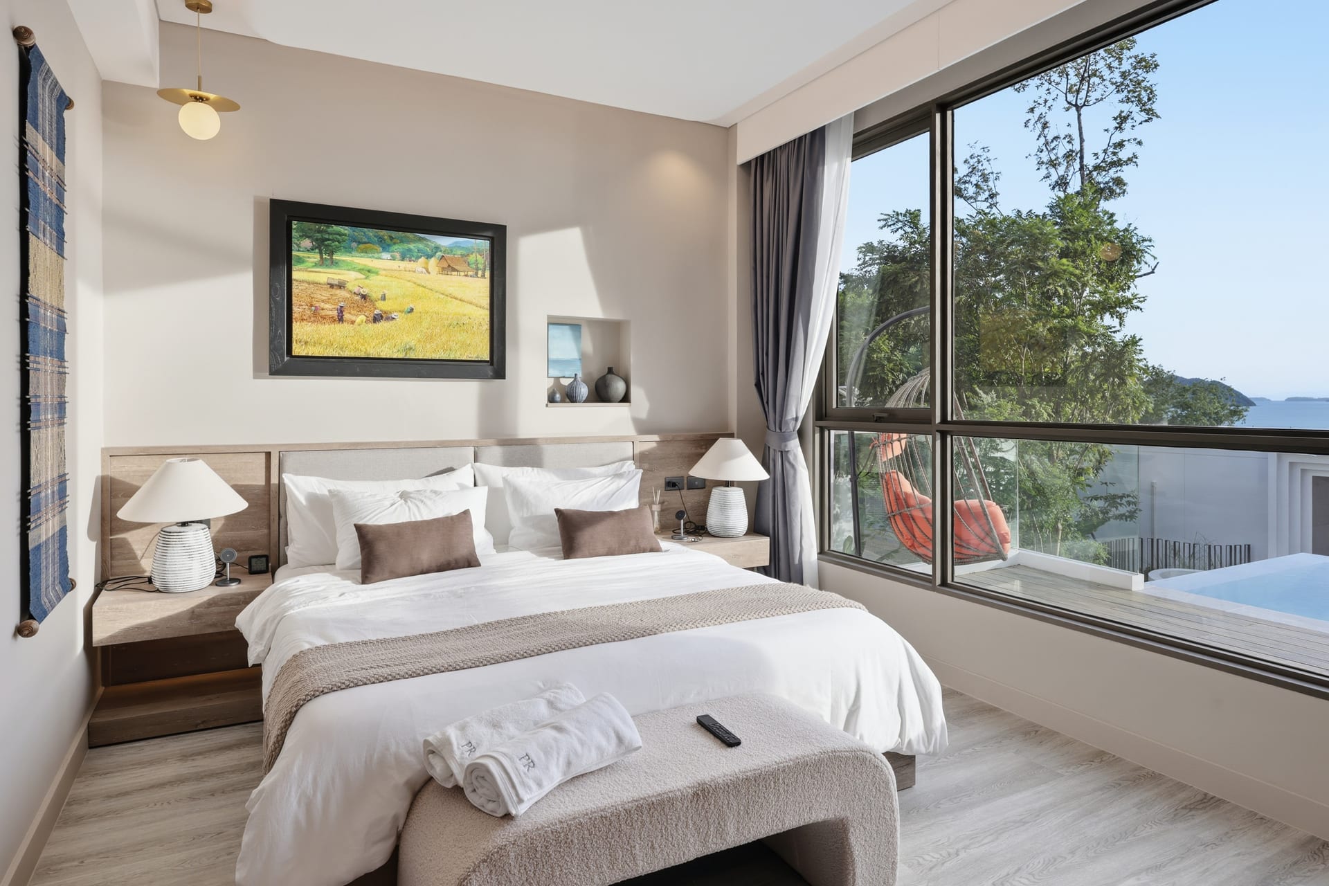 The primary bedroom with king bed and a framed Chootoun landscape above the headboard, sea view through the window