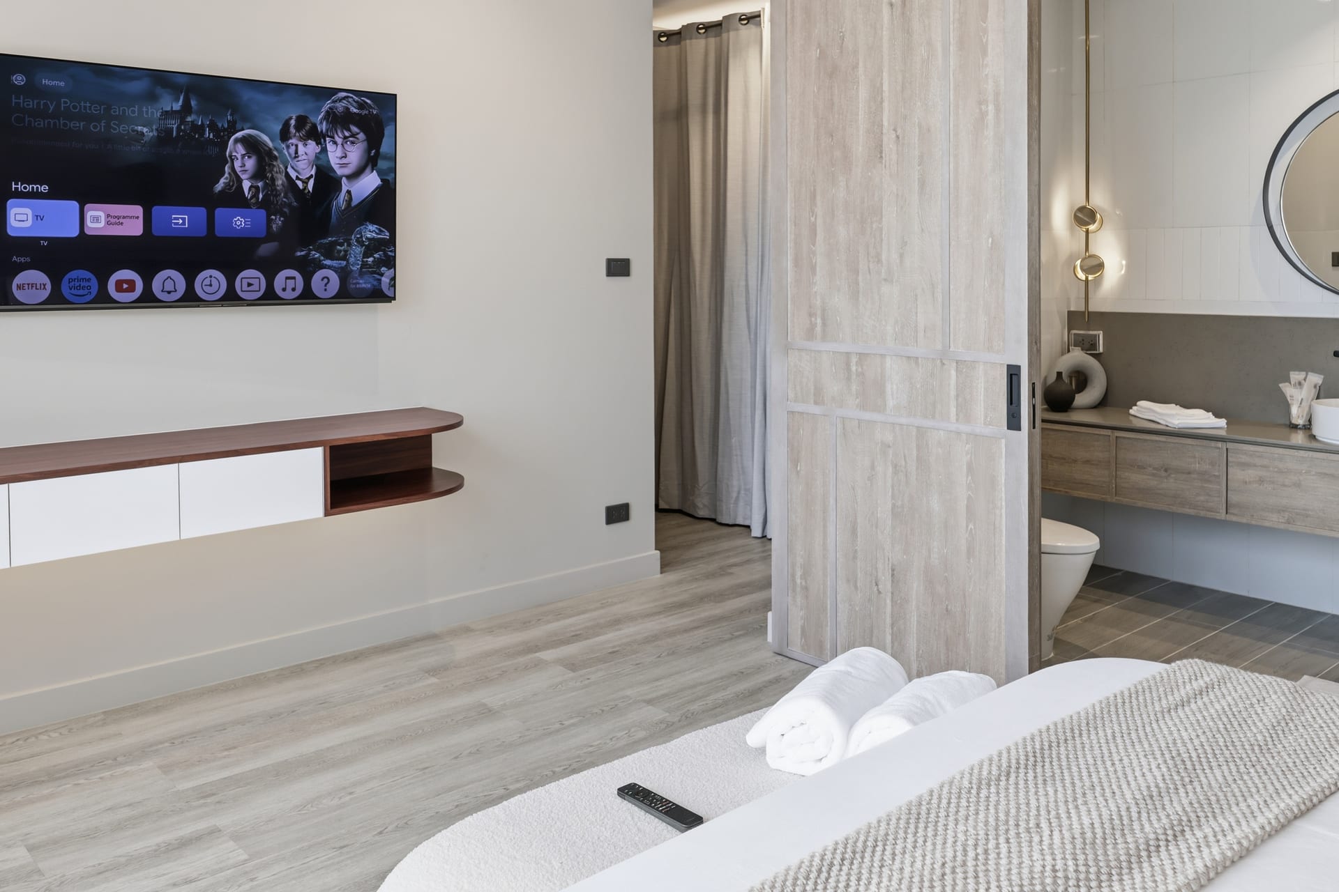 The primary bedroom with wall-mounted TV and a glimpse through to the ensuite bathroom, fresh towels on the bed