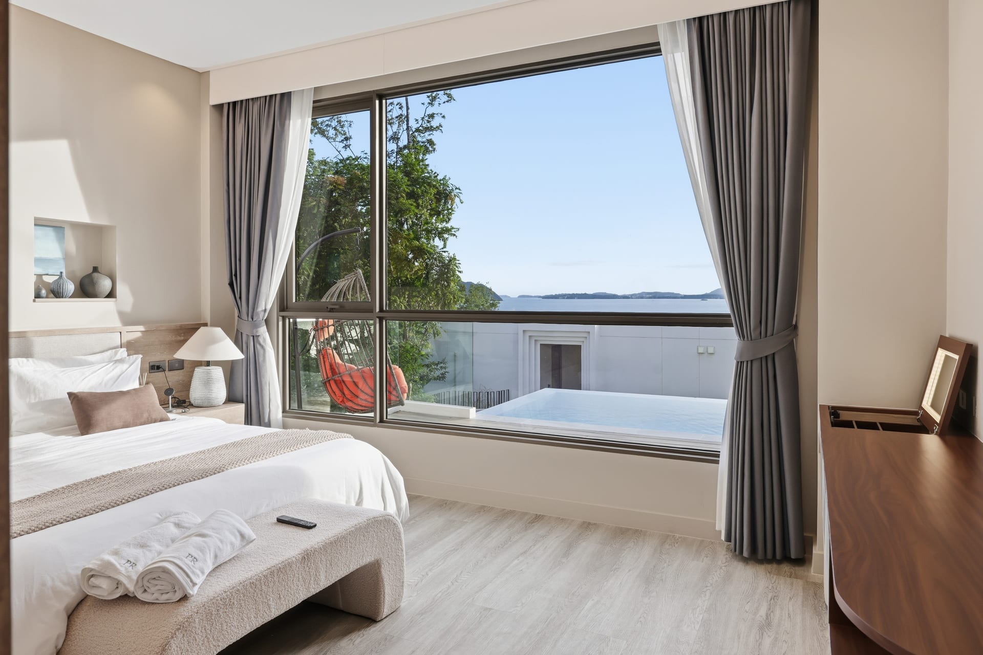 The primary bedroom with a cushioned window seat and desk beside the full-height glass, the bay beyond