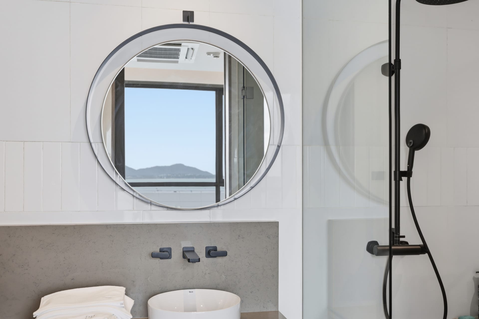 The primary bathroom's double vanity with twin round mirrors and a porthole window, walk-in shower alongside