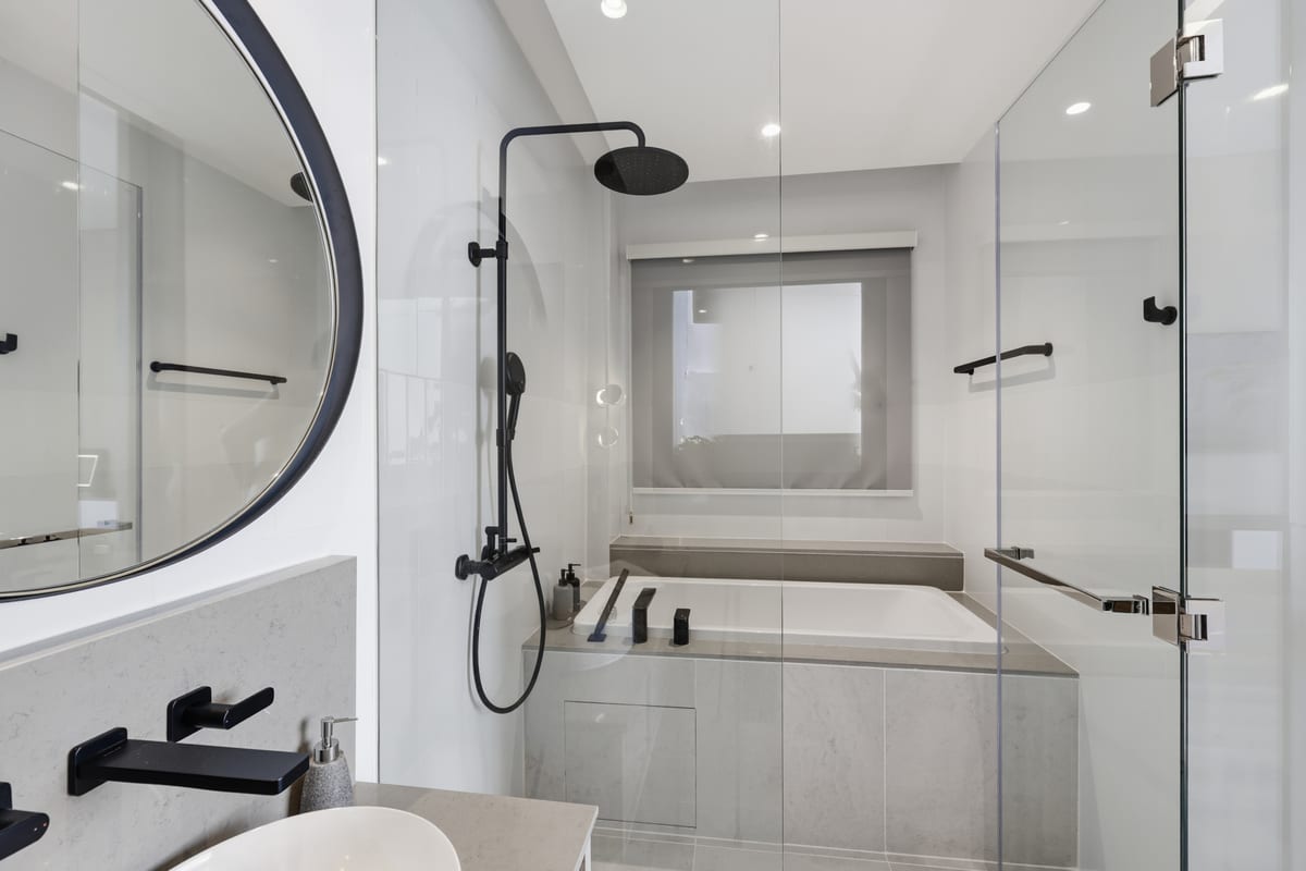 The primary bathroom with a deep soaking tub, a glass rainfall shower and a round mirror