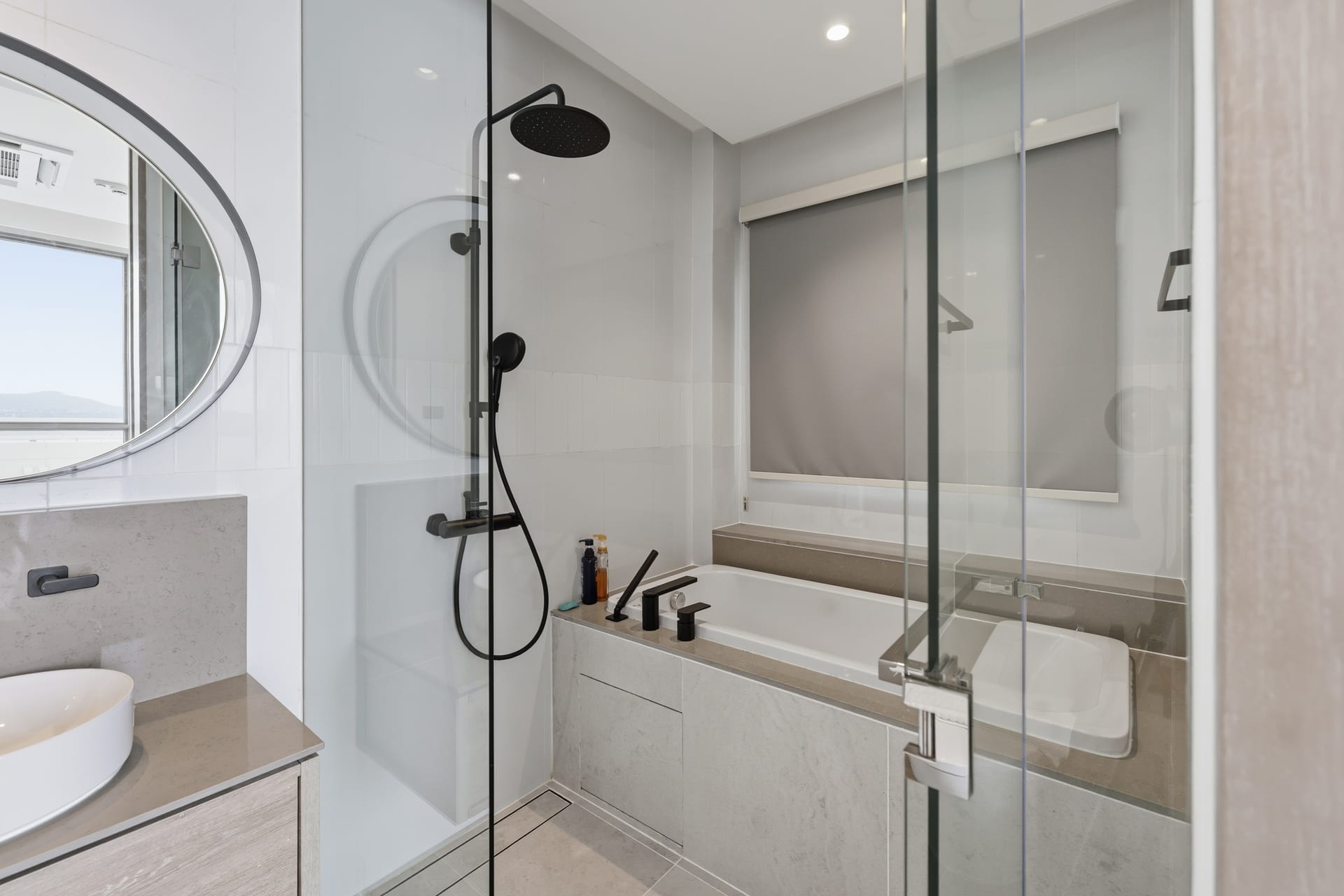 The primary bathroom's glass walk-in rainfall shower beside the soaking tub, round mirror above the vanity