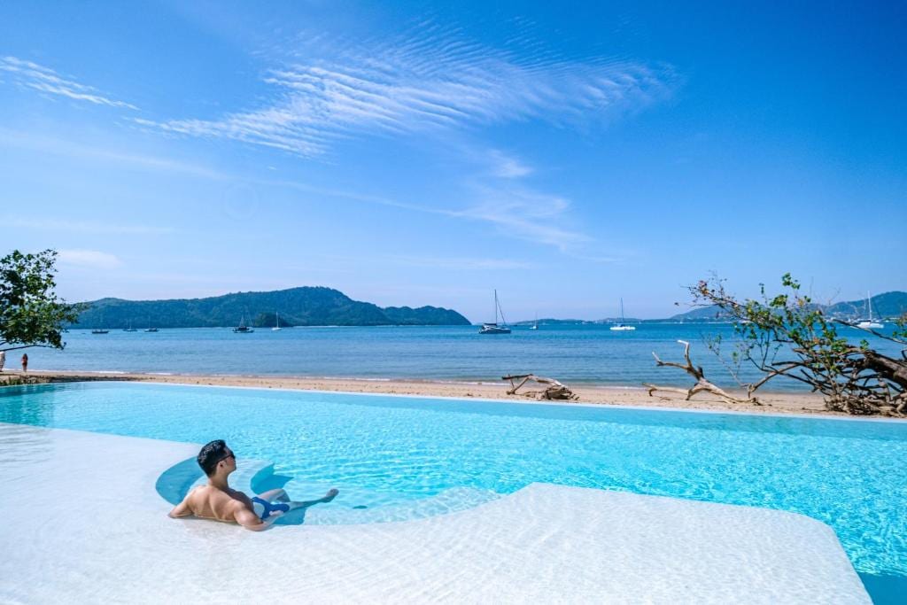 Daytime view of the Veranda Resort beachfront pool with a swimmer and longtail boats on the Andaman