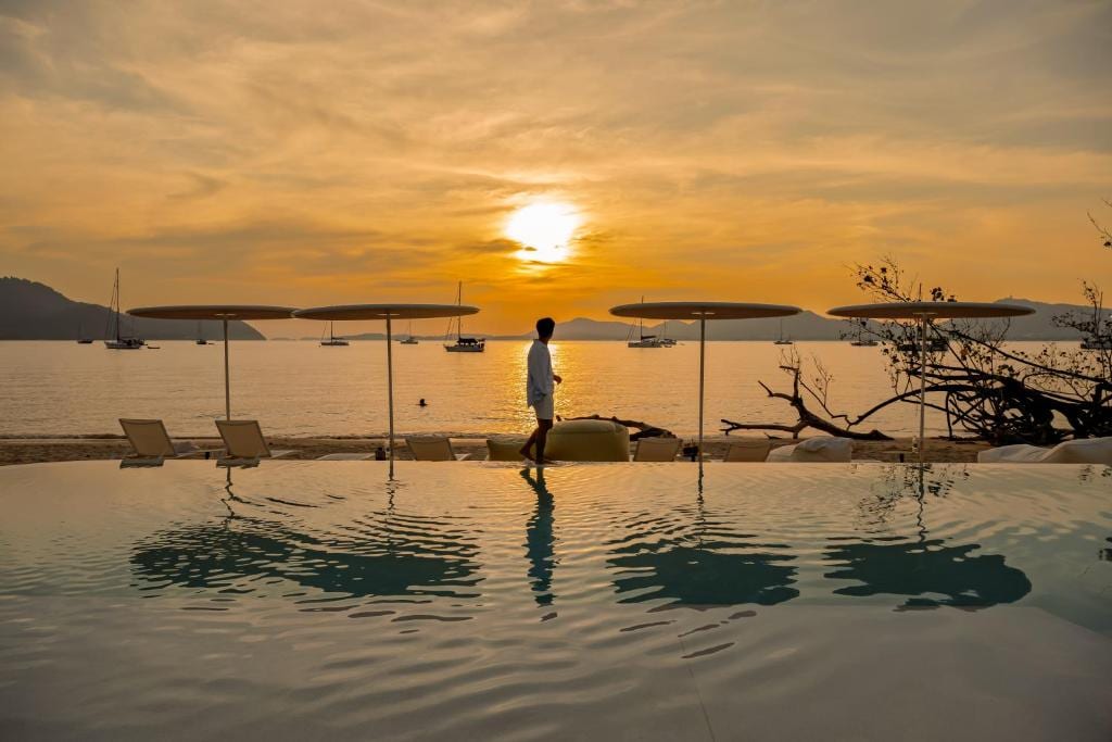 The Veranda Resort beachfront pool at sunset — a guest standing at the infinity edge, longtail boats in the bay
