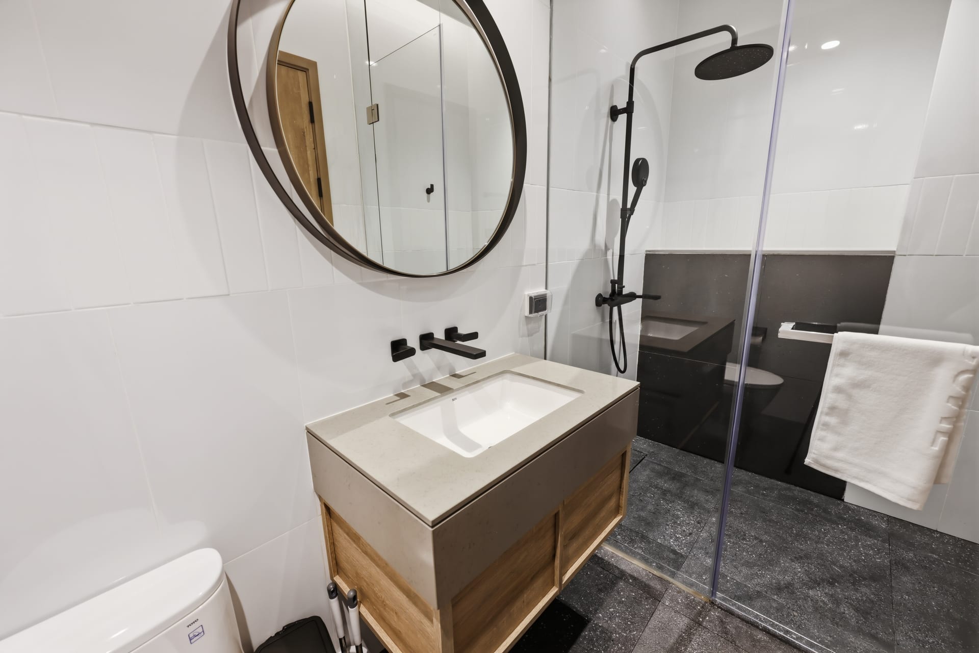 The second bathroom's wood vanity and round mirror with the walk-in shower behind
