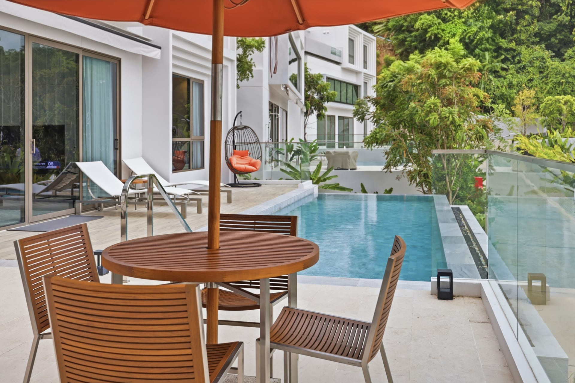 Wide terrace view with a daybed and orange parasol beside the infinity pool, the bay and Cape Panwa hills behind