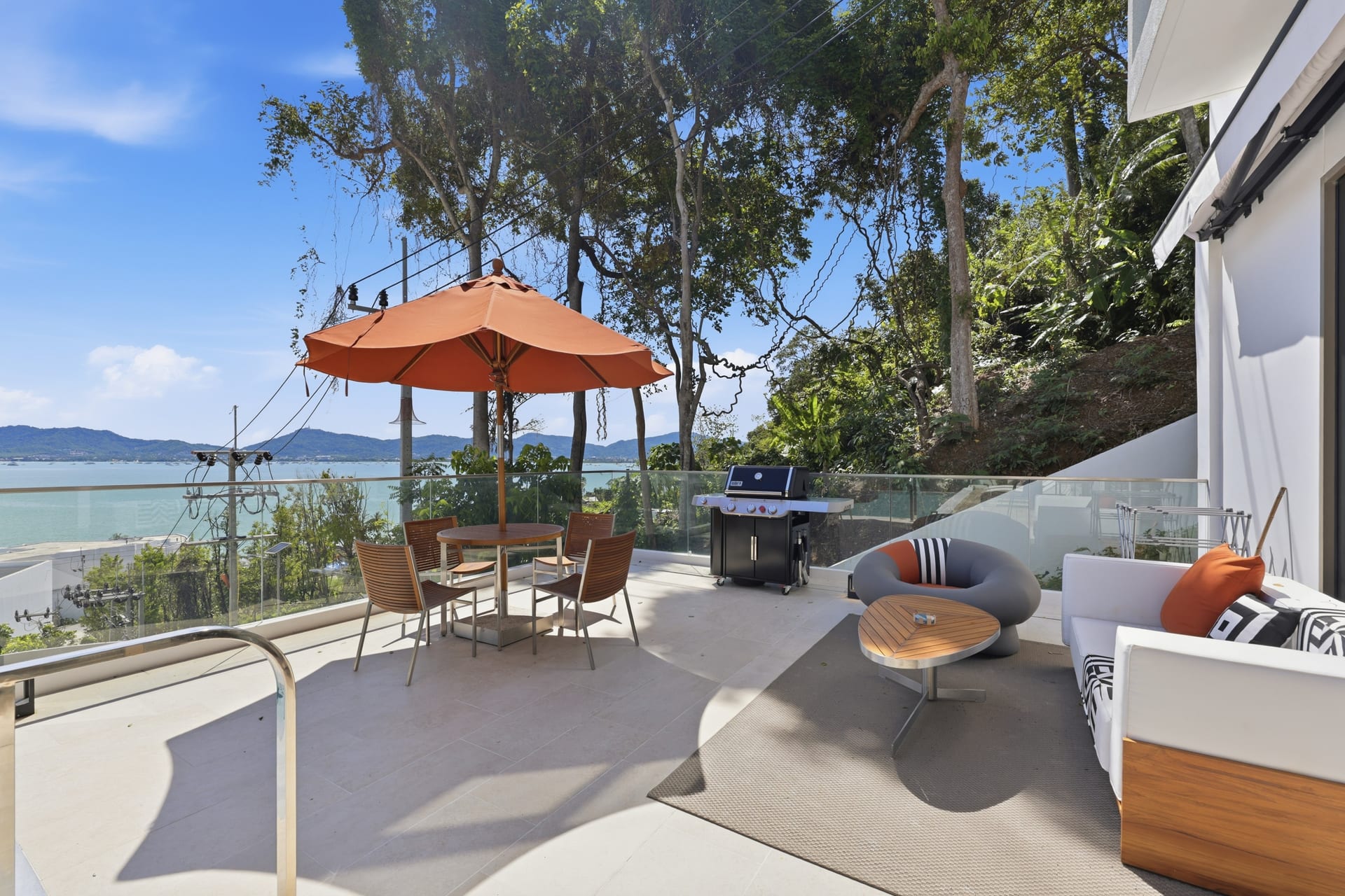 The terrace set for the evening — dining table, firepit and lounge seating under an orange parasol, the bay beyond