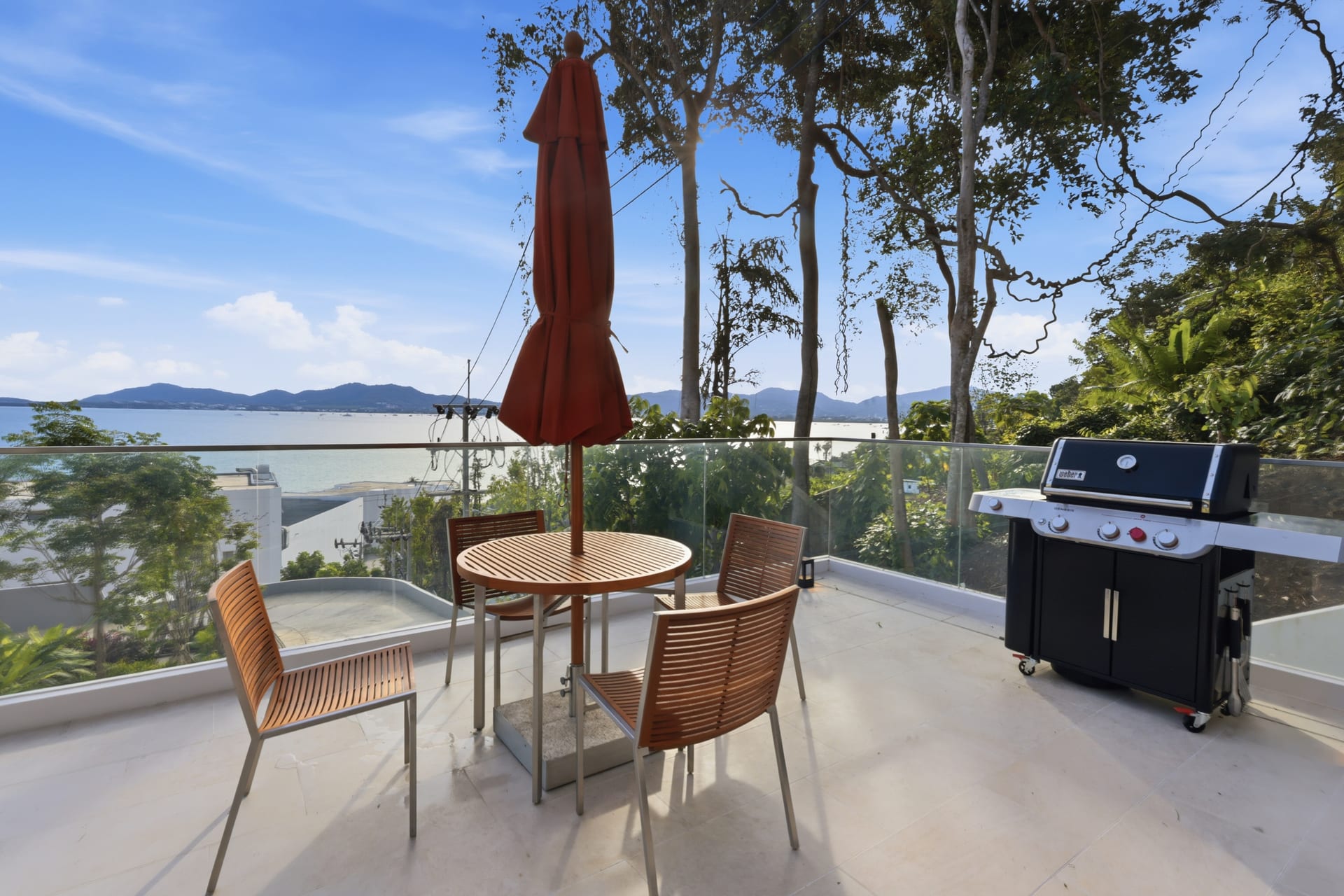 The terrace dining table set beside the gas grill under an orange parasol, the bay and headlands behind