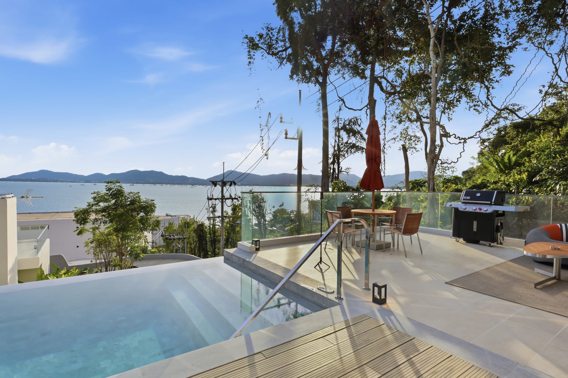 The terrace's glass railing with a rounded pod chair, looking out over the infinity pool and the bay