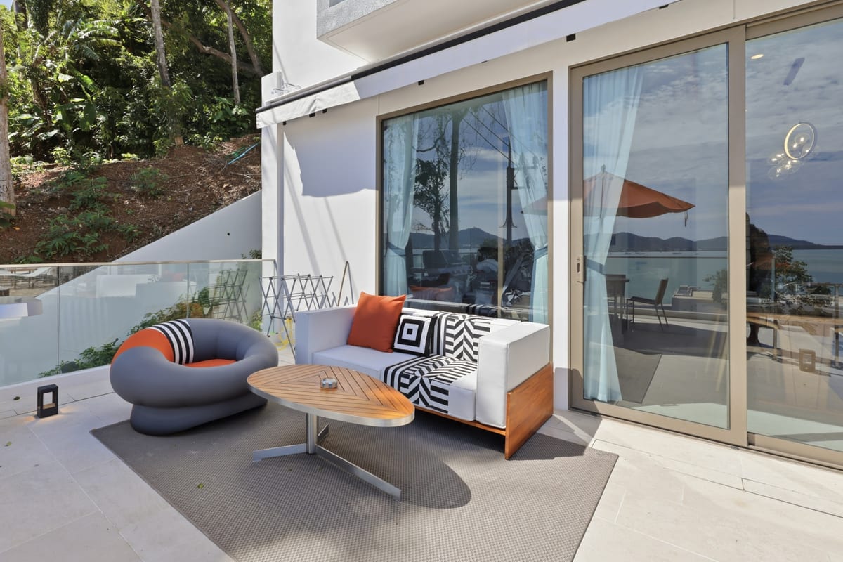 Terrace lounge with an outdoor sofa, a rounded pod chair and a firepit table, sliding doors back into the suite and the bay beyond