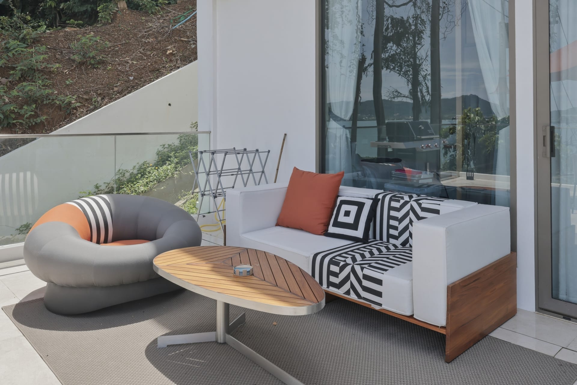 Terrace lounge seating — a rounded pod chair, an outdoor sofa and a teak table, the bay beyond